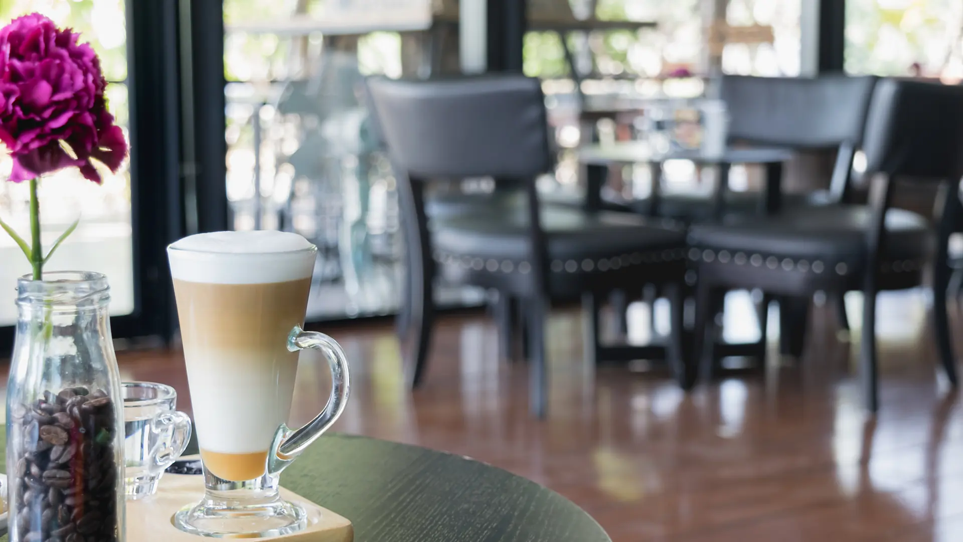 Le salon vide le matin : un latte sur un guéridon, les chaises et les fenêtres derrière