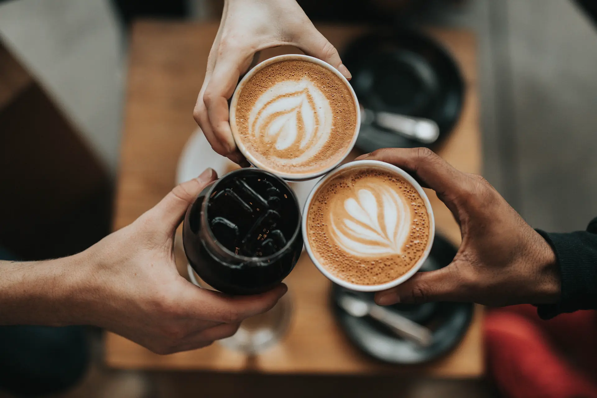Trois mains rapprochent deux lattes et un café glacé au-dessus de la table