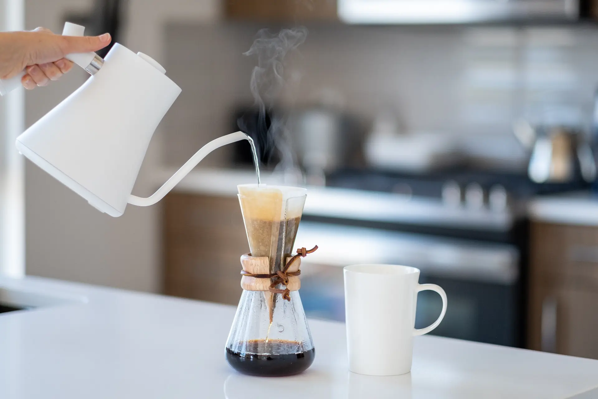 La bouilloire blanche verse l’eau dans une Chemex, la vapeur monte