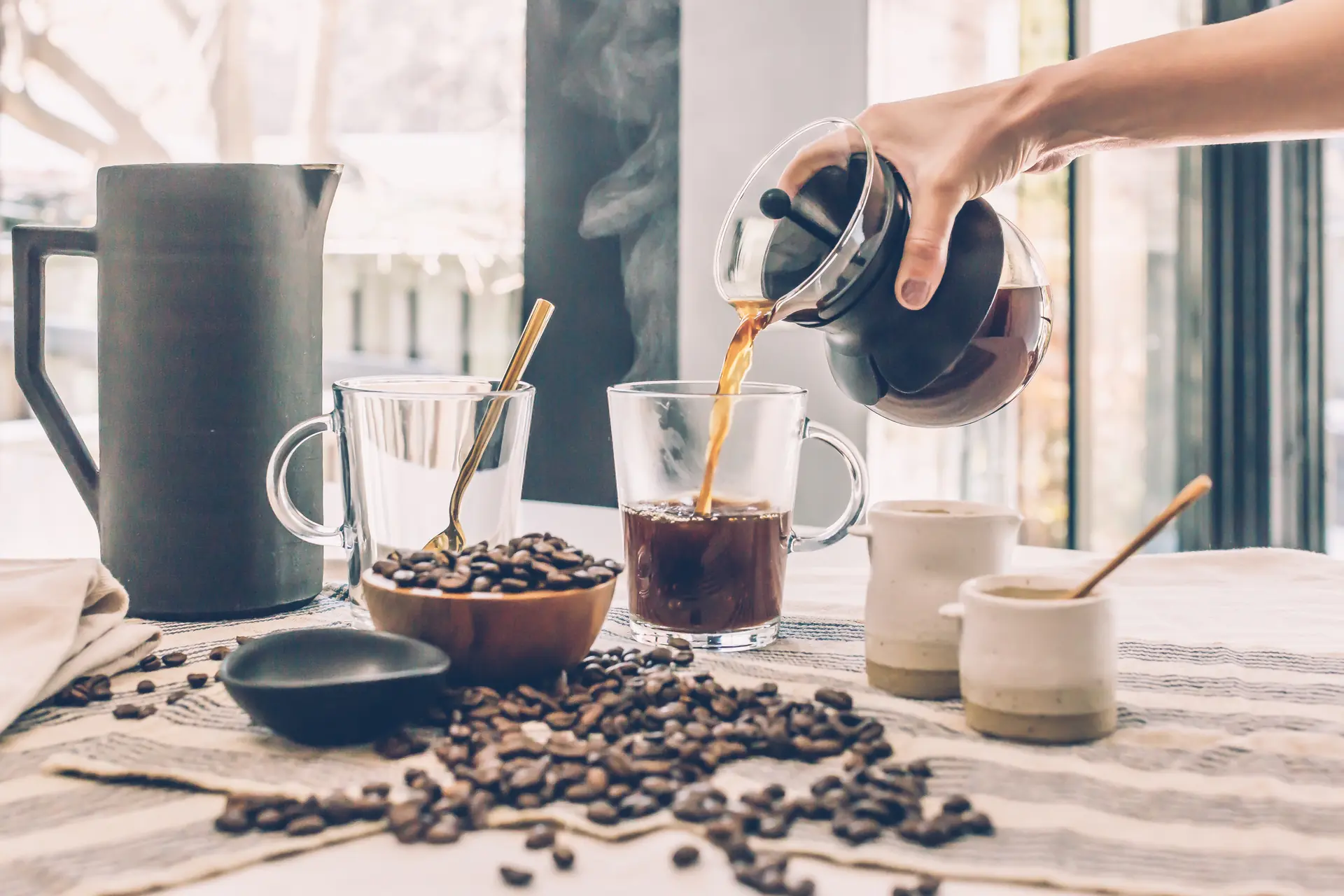 Le café versé de la carafe dans une tasse de verre, des grains sur la nappe
