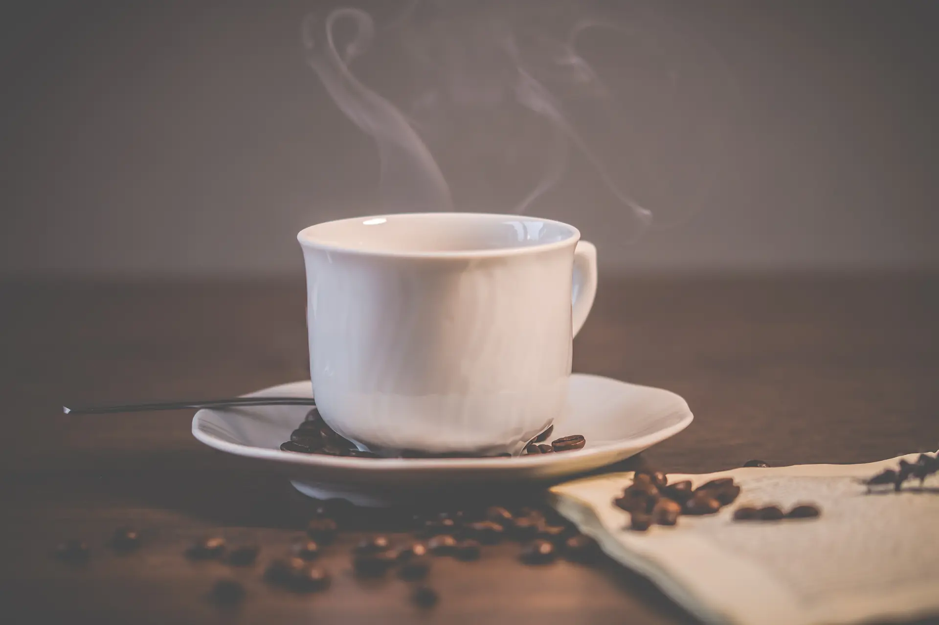 Une tasse blanche qui fume, des grains et un livre ouvert